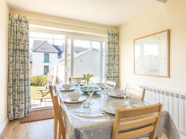 A dining room with a table set for six near sliding glass doors with curtains at The Holiday House 2 Atlantic Mews in Polzeath
