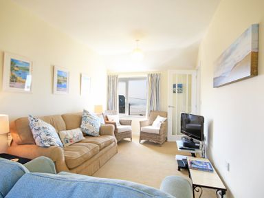 A living room with two wicker chairs a beige sofa a blue armchair a small television on a stand and framed pictures on the wall at The Holiday House 2 Atlantic Mews in Polzeath