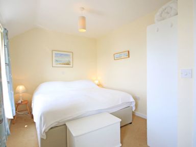 A bedroom with a white bedspread two lamps a chest and framed pictures on the wall at The Holiday House 2 Atlantic Mews Polzeath