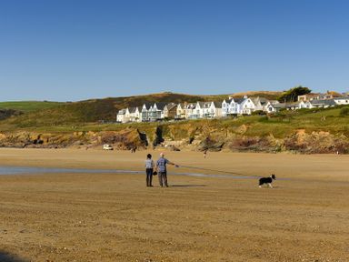 A beach with people walking a dog and houses on a hill in the background at The Holiday House (2 Atlantic Mews) in Polzeath