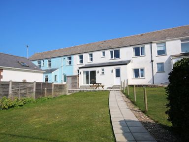 A pathway leading to the back door of a row of houses with a picnic table on the patio at The Holiday House (2 Atlantic Mews) in Polzeath