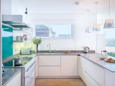 A kitchen with white cabinets a stove a microwave a sink and hanging lights at Stepper Point in Polzeath