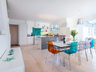 A modern kitchen and dining area with colorful chairs and a dining table set for a meal at Stepper Point in Polzeath
