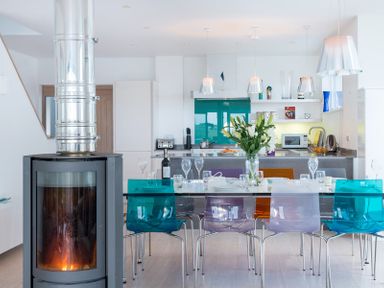 A kitchen and dining area with colorful chairs a glass table and a wood stove at Stepper Point Polzeath