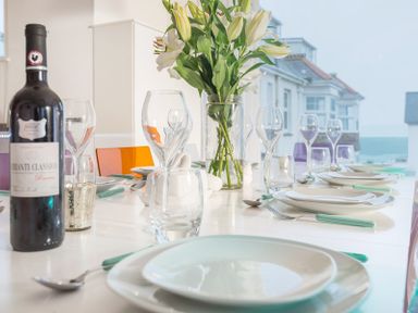 A dining table set with wine glasses plates utensils and a bottle of wine with flowers in a vase at Stepper Point in Polzeath