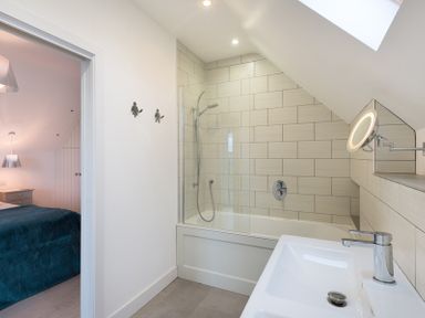 A bathroom with a bathtub and shower next to a sink with a faucet and a round illuminated mirror at Stepper Point in Polzeath