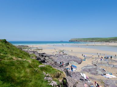 A beach scene with people on sand and rocks near the ocean at Stepper Point in Polzeath