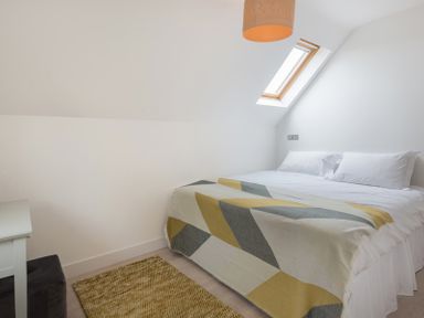 A bedroom with a bed a geometric patterned throw a skylight and a rug at Stepper Point in Polzeath