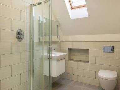 A bathroom with a glass shower enclosure a wall-mounted sink a toilet and a skylight window at Stepper Point Polzeath
