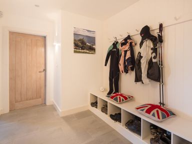A mudroom with a wooden door coats wetsuit walking sticks and boots on cubby shelves at Stepper Point Polzeath