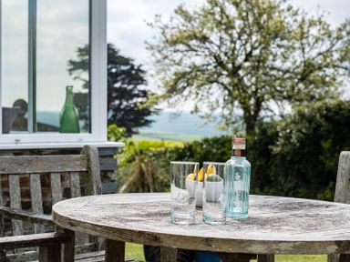 An outdoor wooden table with two glasses a bottle and a bowl of fruit in a garden at Corriana in Rock