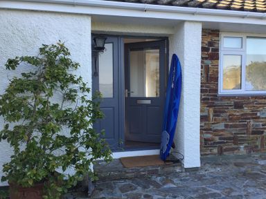 A front door with a blue surfboard leaning against the wall and a potted plant beside it at Corriana in Rock