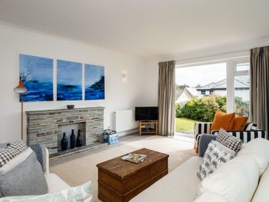 A living room with a wooden chest coffee table a stone fireplace and a glass door opening to a garden at Corriana Rock