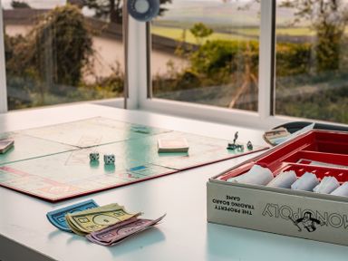 A Monopoly board game set up on a white table near a window with game pieces and cards at Corriana in Rock