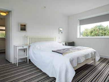 A bedroom with a white bed and bedside tables next to a window with a gray blind at Corriana in Rock
