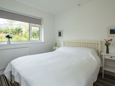 A bedroom with a bed covered in a white bedspread two bedside tables with flowers and lamps and a window with a gray blind at Corriana in Rock