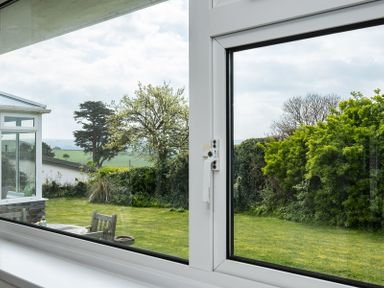 View of a garden with grass, trees, bushes, and wooden chairs seen through a window at Corriana in Rock