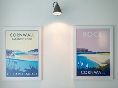 Two framed posters of Cornwall landscapes on a wall under a single wall light at Corriana Rock