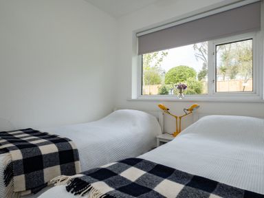 A bedroom with two single beds covered with white bedspreads and plaid blankets with a window showing a garden outside at Corriana in Rock