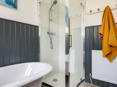 A bathroom with a white bathtub a glass shower enclosure with a showerhead a mustard towel hanging on a hook and a white radiator Corriana Rock