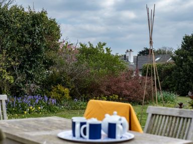 A garden with wooden chairs and a table set with a teapot and cups at Corriana Rock