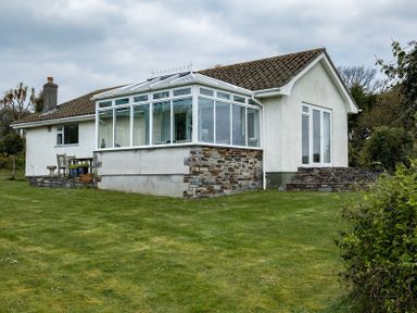 A white bungalow house with a glass conservatory and garden furniture on a lawn at Corriana in Rock