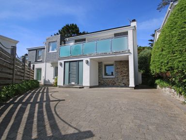 A modern two story house with a paved driveway a glass balcony and surrounding trees at Drifters Rock