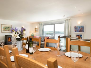 A dining table set with plates wine glasses and flower vase near a living room with sofa and large window showing a water view at Drifters in Rock
