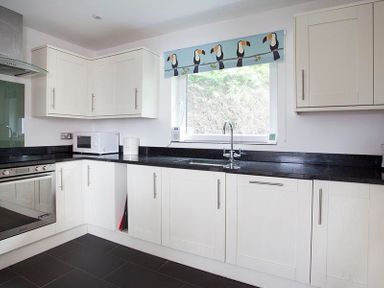 A kitchen with white cabinets black countertop microwave oven and window with bird patterned blind at Drifters in Rock