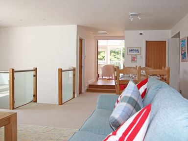 A living room with a blue sofa and striped cushions a dining table with chairs and glass railing at Drifters in Rock