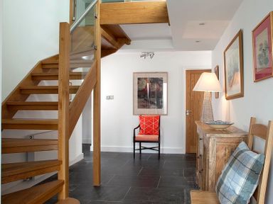 A hallway with wooden stairs a chair with a red cushion a wooden cabinet with a lamp and framed pictures on the wall at Drifters Rock