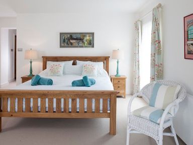 A bedroom with a wooden bed with white and floral bedding two bedside tables with lamps a white wicker chair and floral curtains at Drifters in Rock
