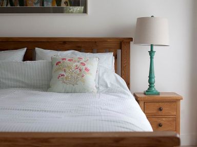 A wooden bed with striped bedding and a floral cushion next to a wooden nightstand with a green lamp at Drifters in Rock
