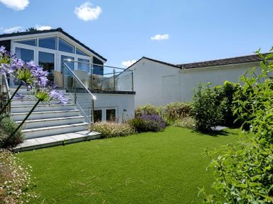 A garden with green lawn and plants in front of a house with steps leading to a glass balcony at Drifters Rock