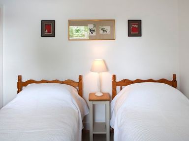 A bedroom with two single wooden beds with white bedding a bedside table with a lamp and three framed pictures on the wall at Drifters in Rock