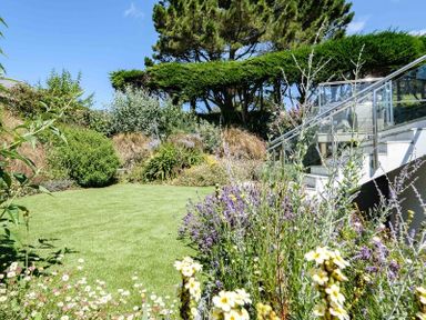 A garden with grass lawn flowers shrubs and a glass railing staircase at Drifters in Rock