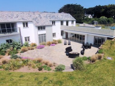A patio area with outdoor seating and plants around a white two story house at Downalong in Daymer Bay