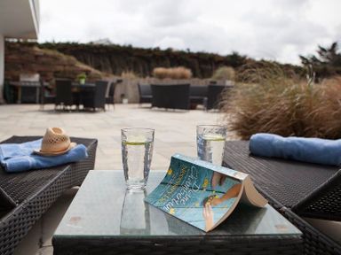 An outdoor patio with two lounge chairs a glass table with two glasses of water and a book at Downalong Daymer Bay