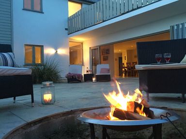 An outdoor patio with a fire pit surrounded by wicker chairs and candles at Downalong in Daymer Bay