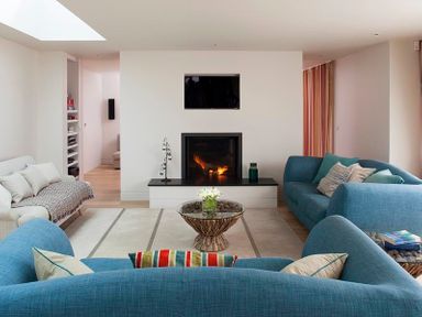 A living room with blue sofas a white sofa a glass coffee table with flowers a fireplace and a wall-mounted tv at Downalong in Daymer Bay