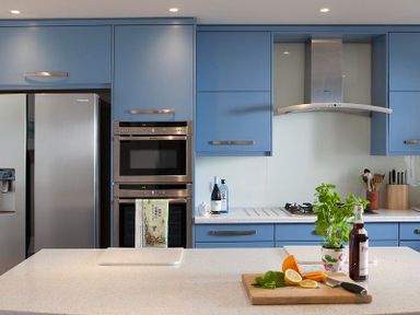 A kitchen with blue cabinets a double oven a stainless steel refrigerator a gas stove and a countertop with a cutting board herbs and fruit at Downalong Daymer Bay