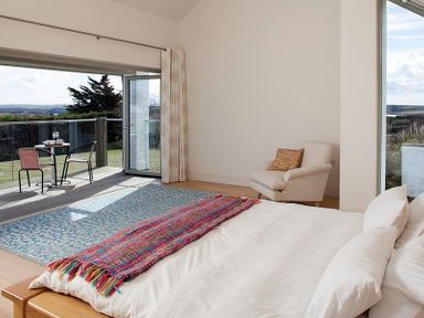 A bedroom with a bed a chair a rug and a small outdoor table with chairs on a balcony at Downalong in Daymer Bay
