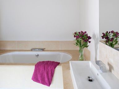 A bathroom with a bathtub holding a purple towel and a sink with a faucet and flowers in a vase next to the bathtub at Downalong in Daymer Bay