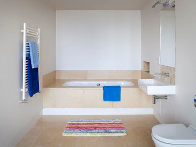 A bathroom with a bathtub a wall-mounted sink a toilet and colorful rug at Downalong in Daymer Bay