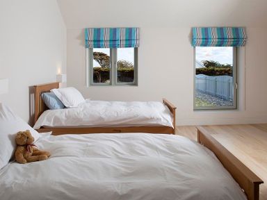 A bedroom with two single beds white bedding blue striped window blinds and a teddy bear on one bed at Downalong in Daymer Bay