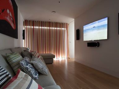 A living room with a sofa and cushions facing a wall-mounted television and striped curtains at Downalong in Daymer Bay
