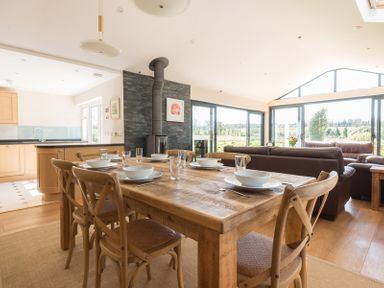 A dining table set with plates bowls and glasses in an open plan kitchen and living area with large windows at Chy-An-Dowr in Rock