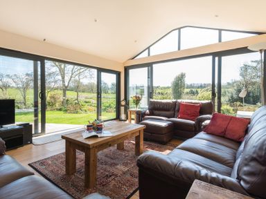 A living room with leather sofas a wooden coffee table and large glass windows overlooking a garden at Chy-An-Dowr in Rock