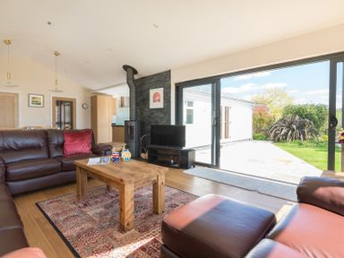 A living room with brown leather sofas a wooden coffee table and large sliding glass doors opening to a garden at Chy-An-Dowr in Rock