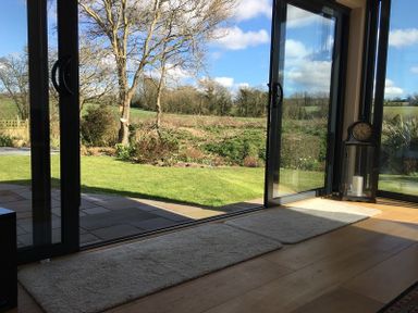 A room with wooden floor and open glass doors overlooking a garden with trees at Chy-An-Dowr in Rock